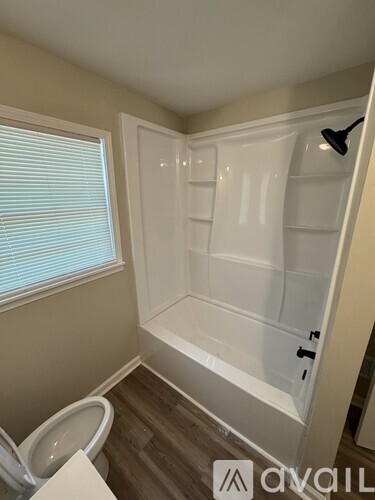 A bathroom with a toilet, a window with blinds, and a walk-in shower.