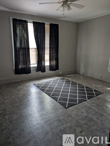 A room with a fan, grey floor, and a window with curtains.