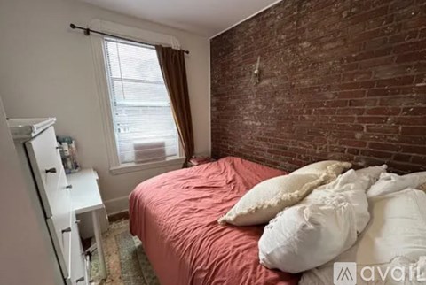 A bedroom with a red bedspread and a white nightstand.