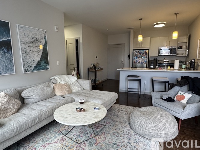 A living room with a grey couch, a coffee table, and a kitchen area in the background.
