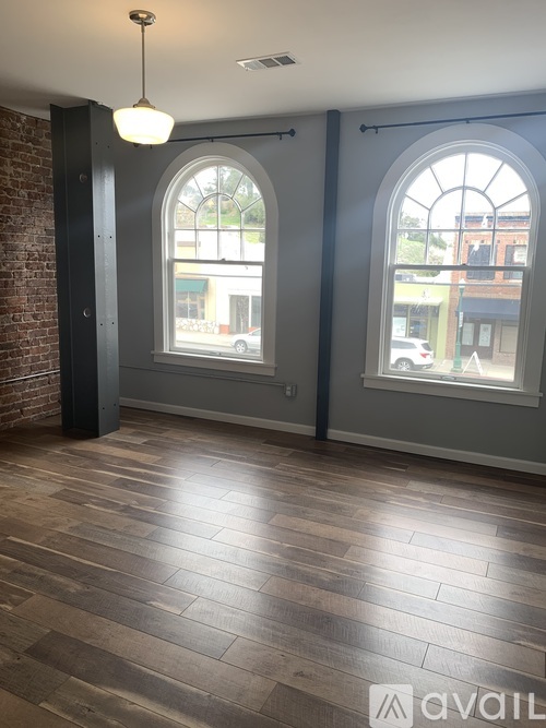 A room with wooden floors and two large arched windows.