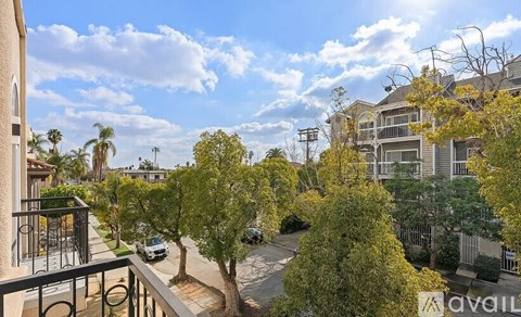 A balcony overlooks a tree-lined street with a car parked on the side.