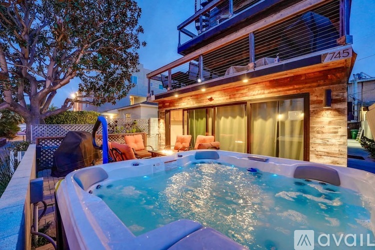 A hot tub is in the foreground of a house with a balcony.