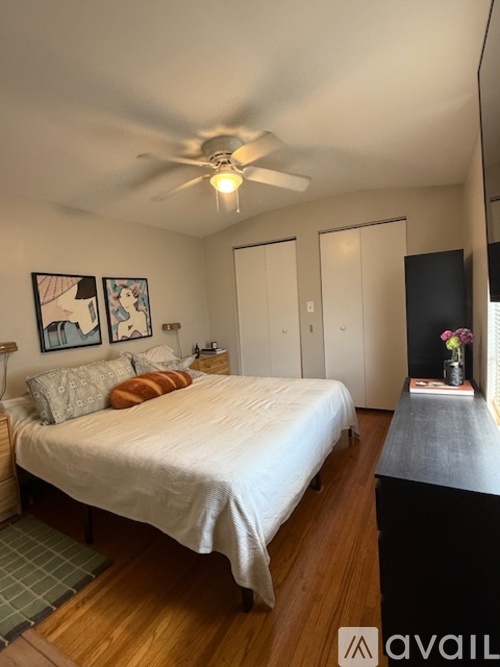A bedroom with a bed, a ceiling fan, and a nightstand with a vase of flowers.