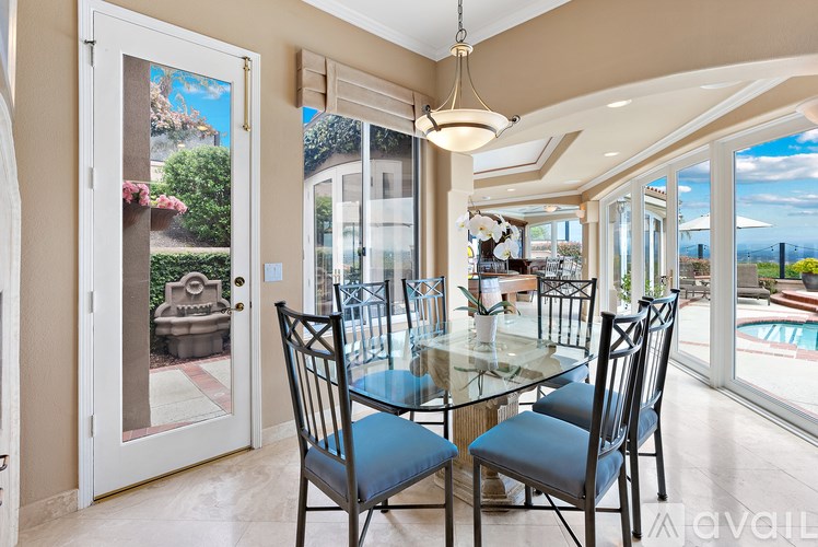A glass table with four chairs in front of a window with a view of a pool and a house.