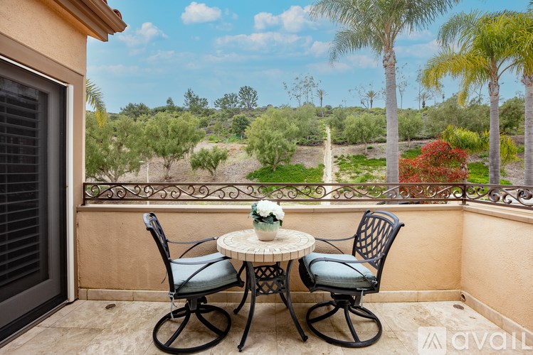 A table with two chairs is on a balcony with a view of a garden.