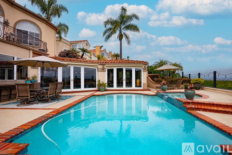 A large swimming pool in a backyard with a patio and chairs.