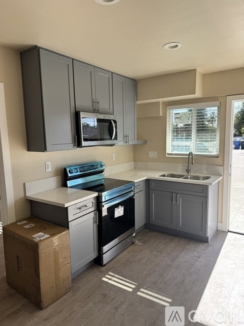 A kitchen with a black fridge and microwave, a white countertop, and a window with blinds.