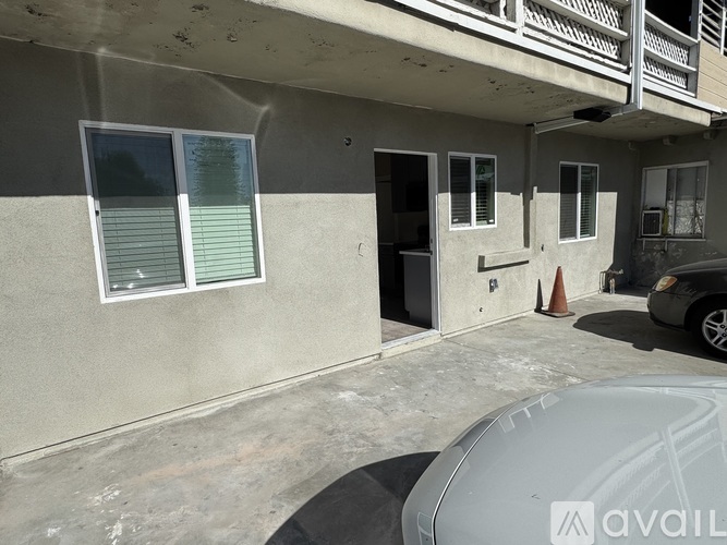 A car is parked in front of a building with a grey wall and a white door.