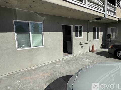 A car is parked in front of a building with a grey wall and a white door.
