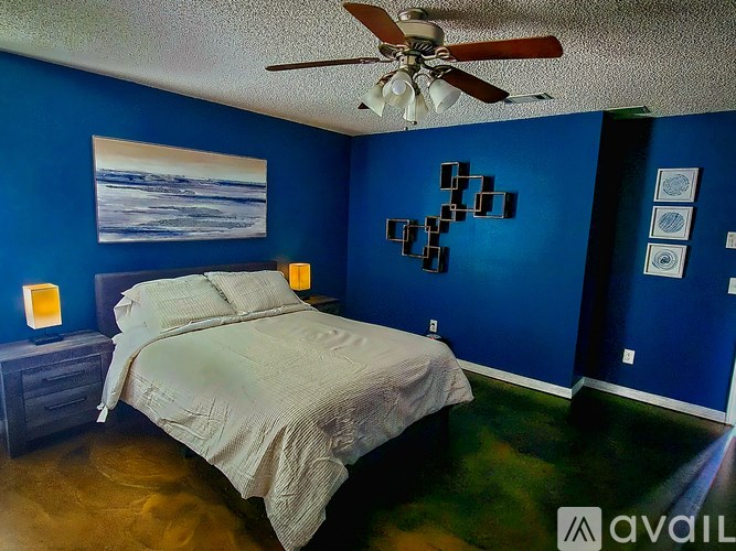 A bedroom with a bed, a ceiling fan, and a painting on the wall.