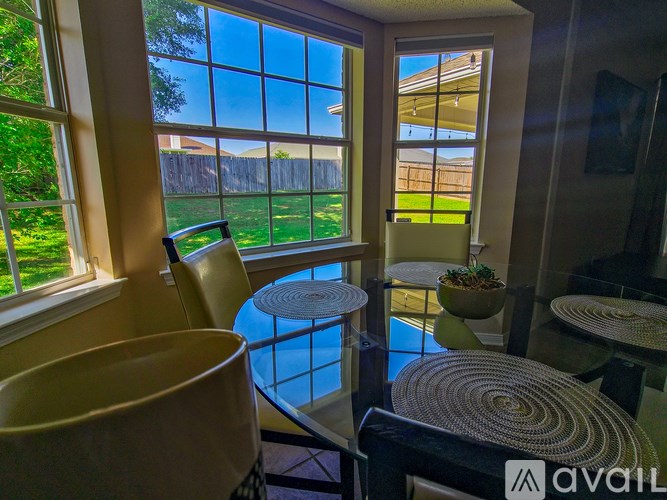 A sunny day outside through the window of a room with a table and chairs.