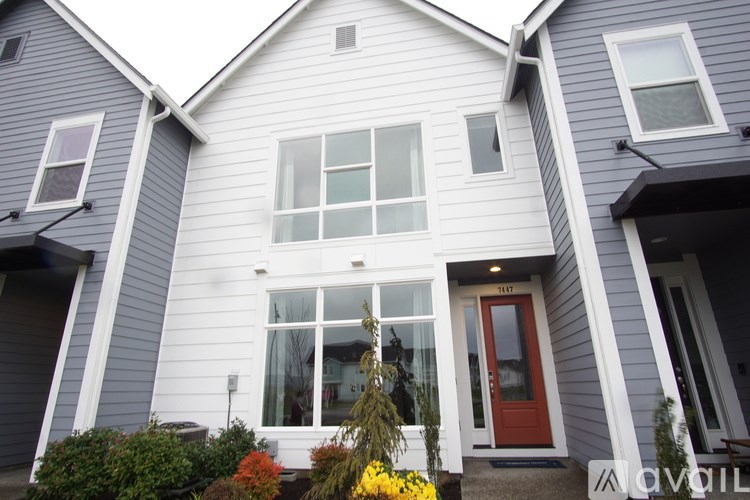 A grey house with a red door and a window with white curtains.