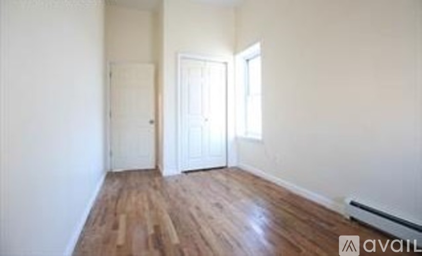 A room with wooden floors and white walls, with a door on the left and a window on the right.