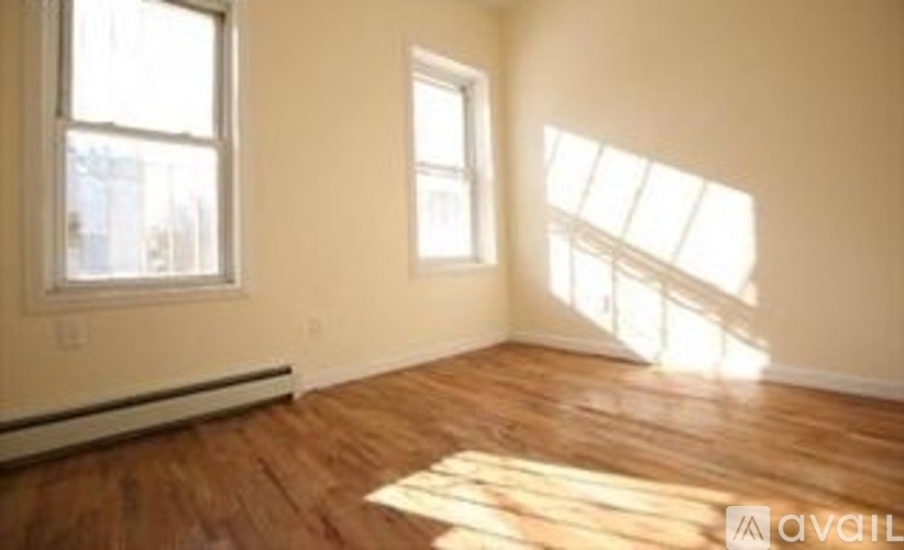 A room with wooden floors and two windows letting in sunlight.