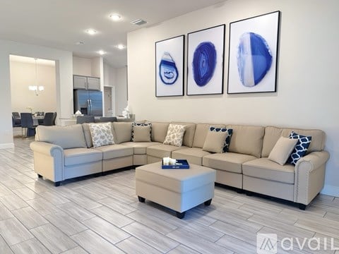 A living room with a beige couch, a coffee table, and three abstract paintings on the wall.