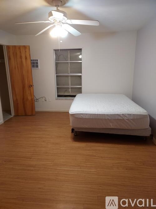 A bedroom with a bed, wooden floor, and a ceiling fan.
