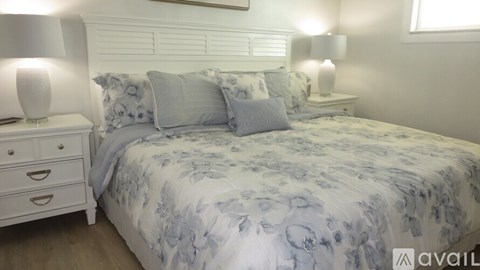 A bed with a blue and white comforter and matching pillows is in a room with two white lamps on either side of the bed.