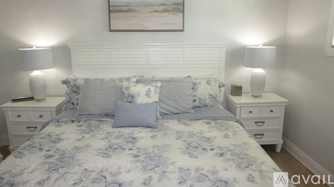 A bed with a blue and white comforter and matching pillows is flanked by two white nightstands with lamps on them.
