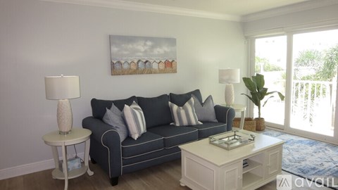 A living room with a grey couch, a white side table, and a painting on the wall.