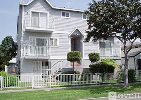 A grey two-story apartment building with a white fence in front.