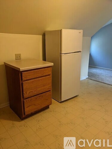 A white refrigerator stands next to a wooden cabinet in a room with a tiled floor.