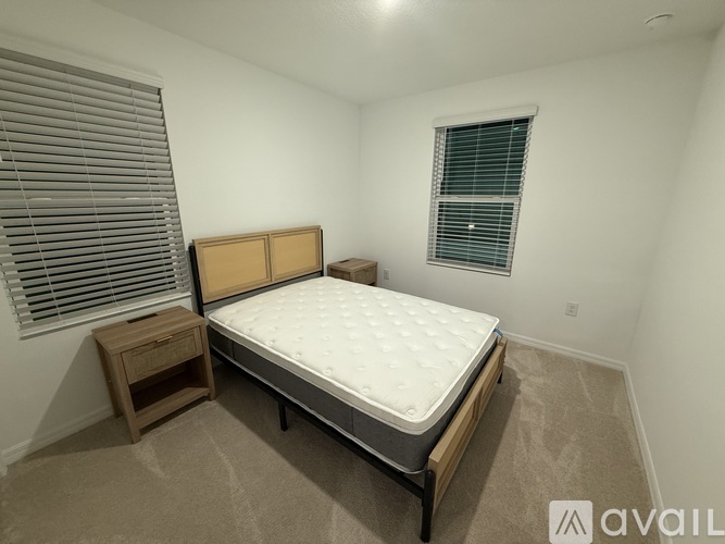 A bedroom with a bed, nightstand, and window with blinds.
