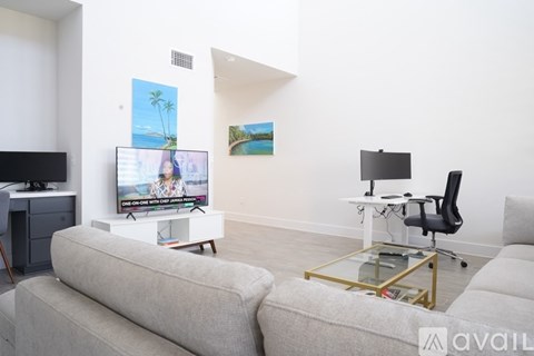 A living room with a grey sofa, a television on a white stand, and a painting on the wall.