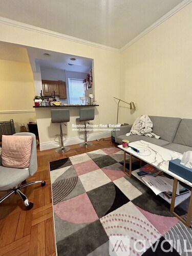 A living room with a grey couch, a pink chair, and a rug with a geometric pattern.