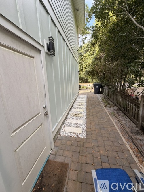A white door with a black handle is on the left side of a brick path.