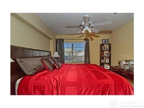 A bedroom with a red bedspread and a ceiling fan.