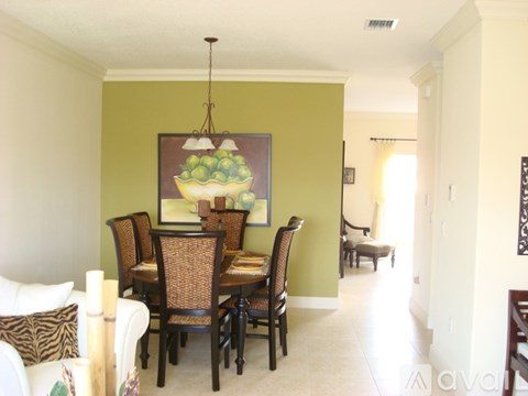 A dining room with a green wall and a painting of a bowl of fruit.