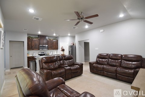 A living room with brown leather furniture and a ceiling fan.