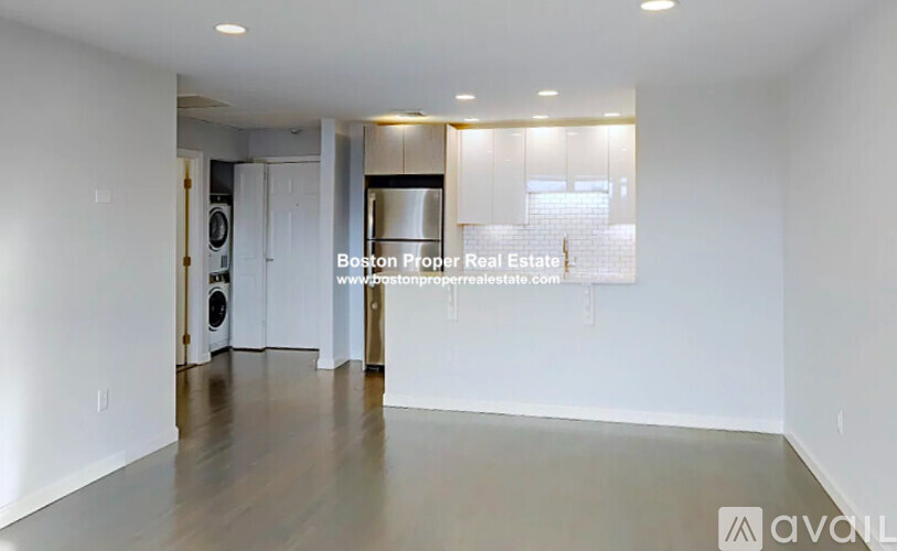 A spacious, empty room with a kitchen area in the background.