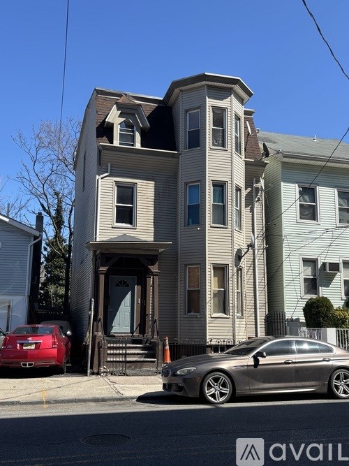 A car is parked in front of a grey two-story house.