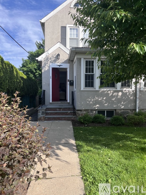 A grey house with a red door and a stone foundation.