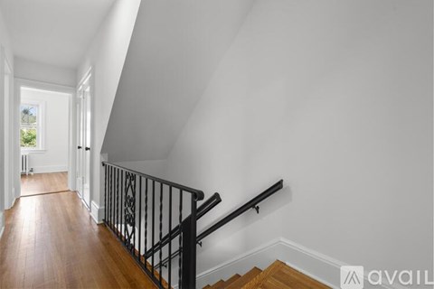 A hallway with a wooden floor and a staircase with a black railing.