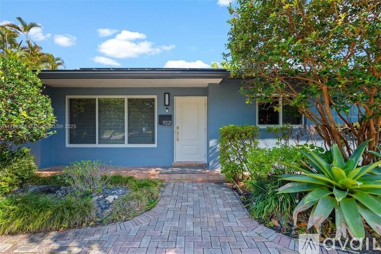 A house with a blue exterior and a white door is surrounded by greenery.