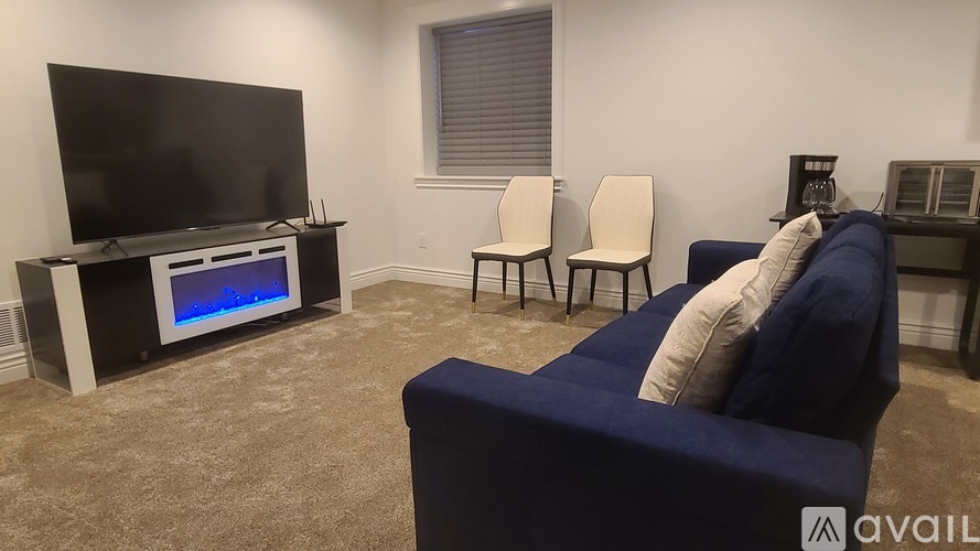 A living room with a blue couch, a television, and two chairs.