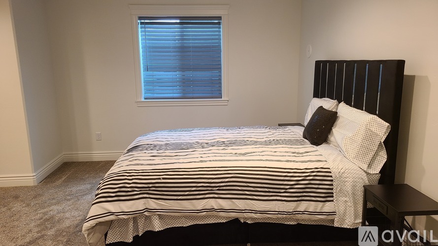 A bedroom with a bed, pillows, and a window with blinds.