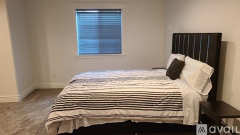 A bedroom with a bed, pillows, and a window with blinds.