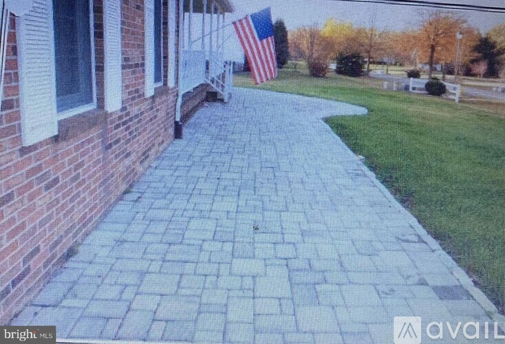 A brick walkway leads to a house with an American flag hanging on the wall.