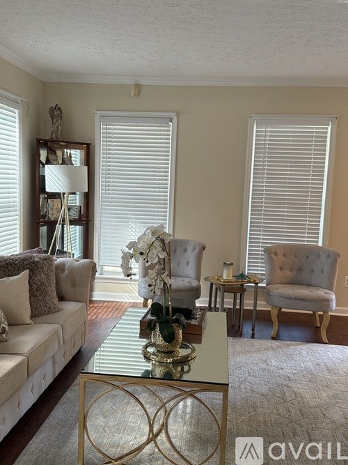 A living room with a white sofa, a grey armchair, and a glass coffee table.