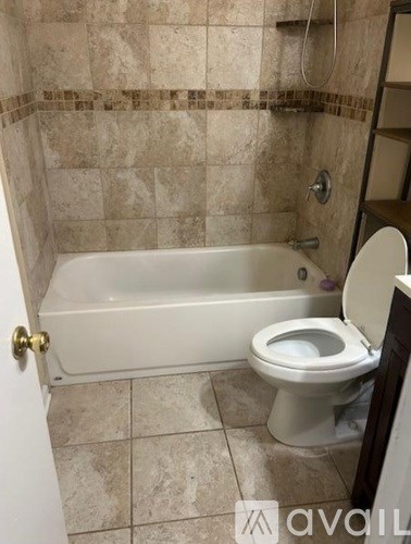 A bathroom with a tiled wall and a white bathtub and toilet.