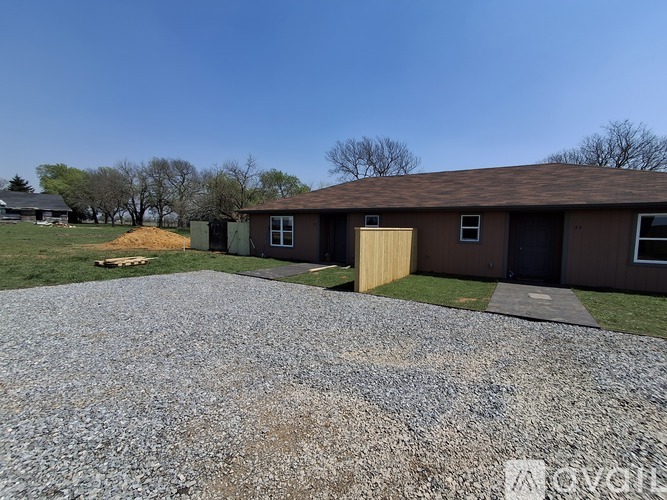 A gravel driveway leads to a brown building with a yellow door.