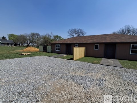 A gravel driveway leads to a brown building with a yellow door.
