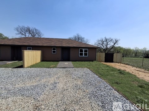 A house with a brown roof and a gravel driveway in front.