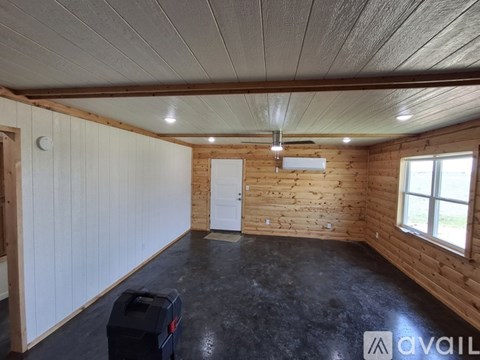 A room with wooden walls and ceiling, a window, and a black trash bin.