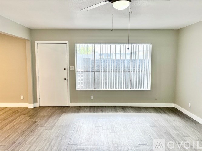 A room with a white door, a window with blinds, and a ceiling fan.