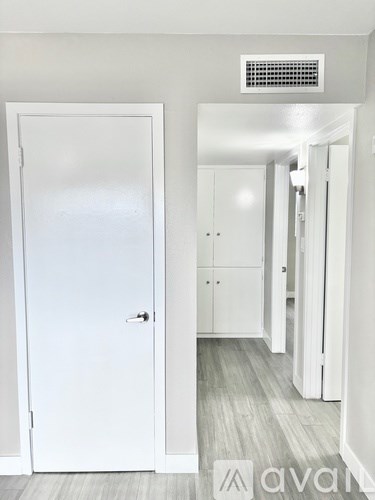 A white door is open to a hallway with a white cabinet and a white wall.